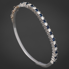 Pulsera rígida en oro blanco de 18kt con frontal orlado de brillantes y zafiros.